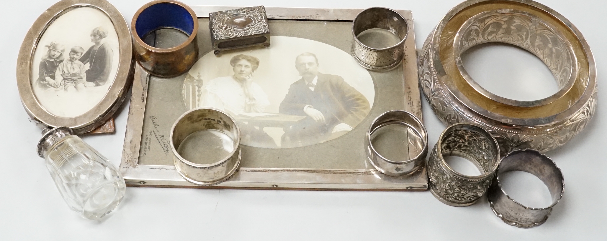 Two George V silver mounted photograph frames including oval, an Indian white metal flower holder and other items including silver napkin rings and a matchbox sleeve.